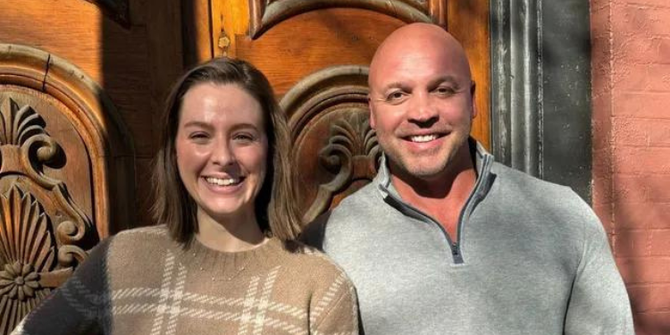 A man and a woman are posing for a picture in front of a wooden door.
