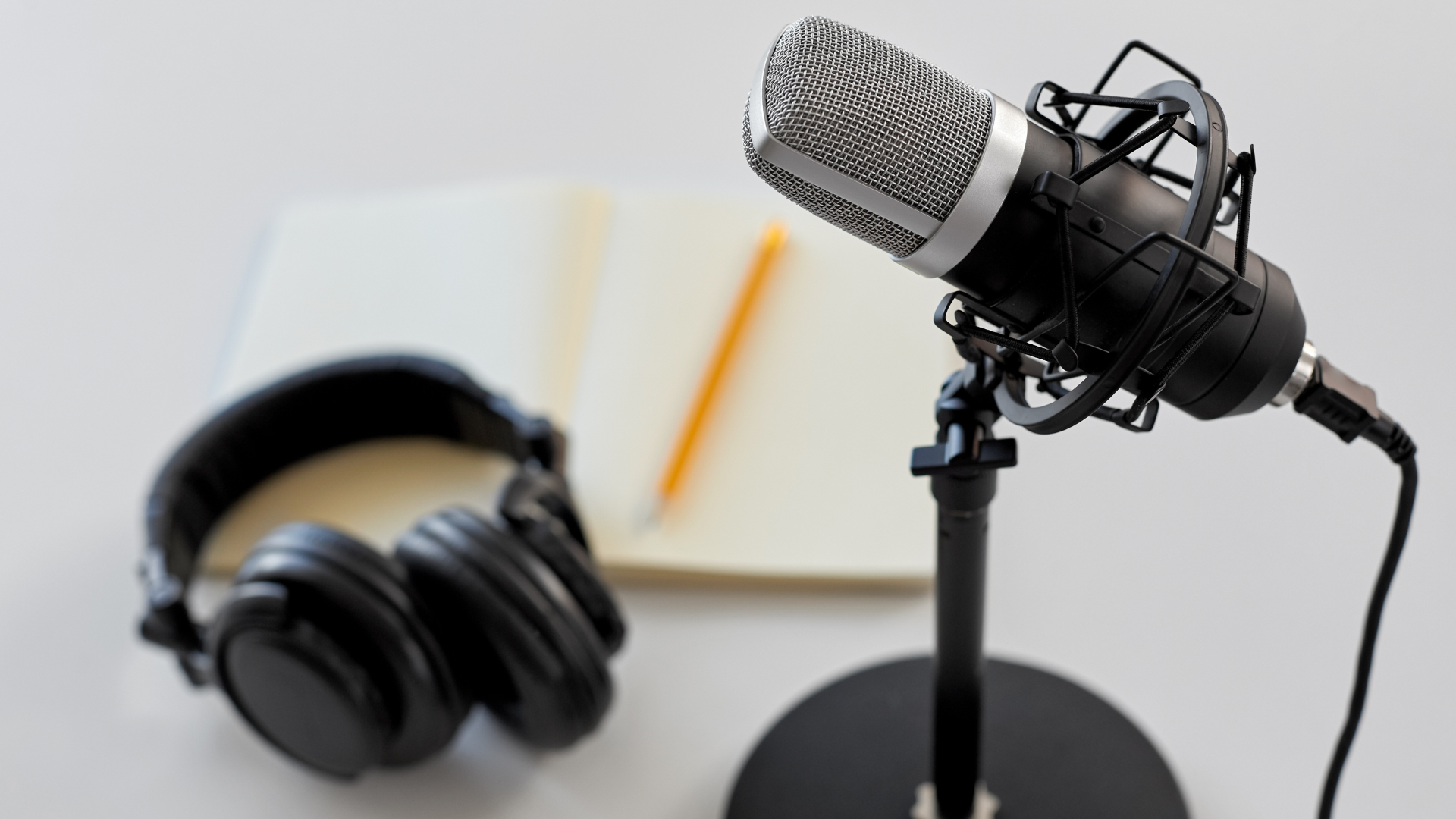 A microphone and headphones are on a table next to a notebook.