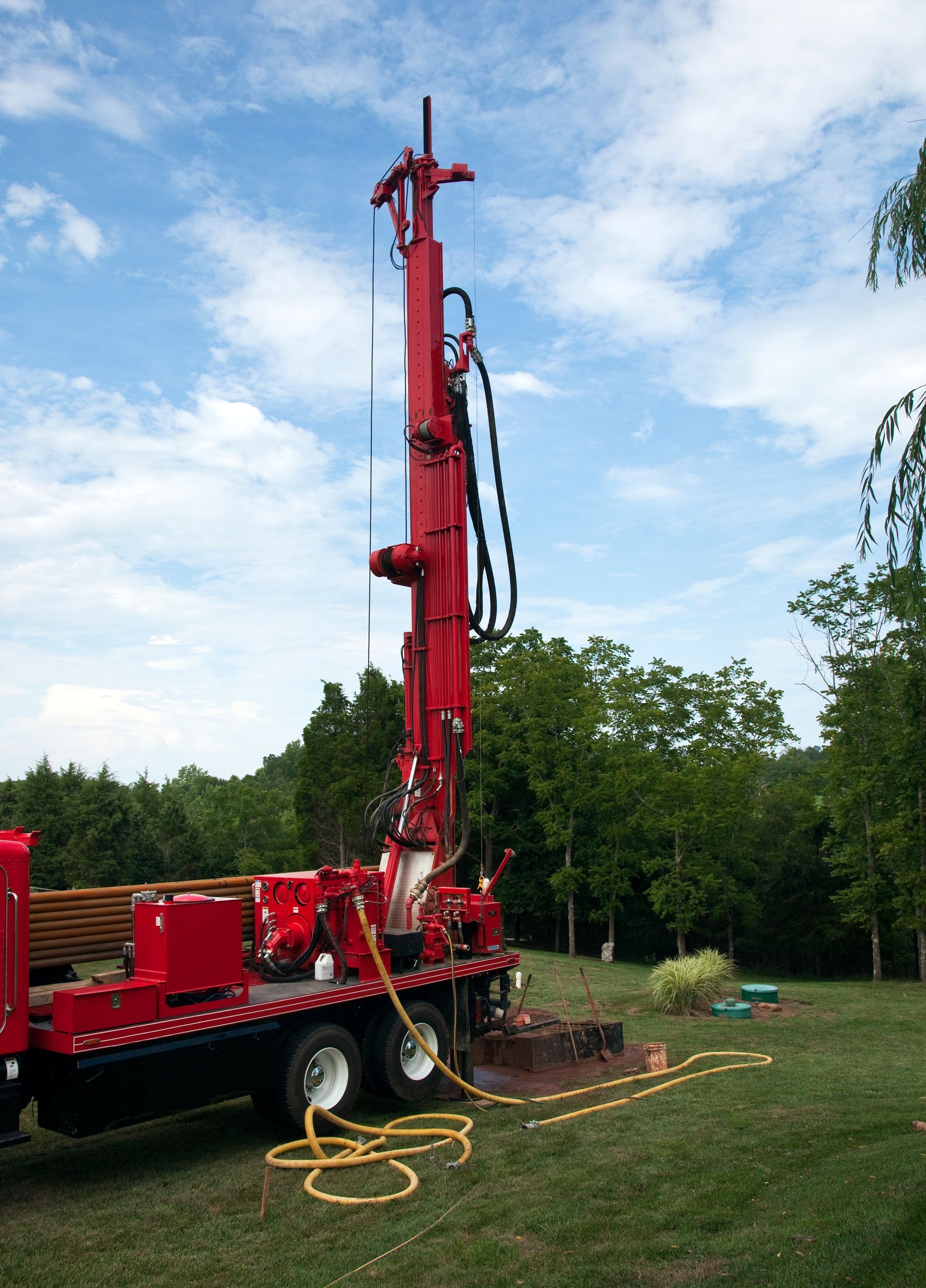 Drilling contractors using a red truck-mounted rig for groundwater drilling in a green outdoor.