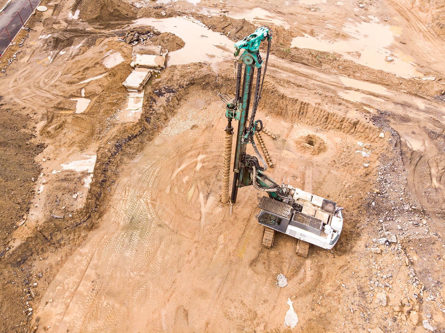 Hydraulic drilling rig installing deep foundation piles at a building construction site.
