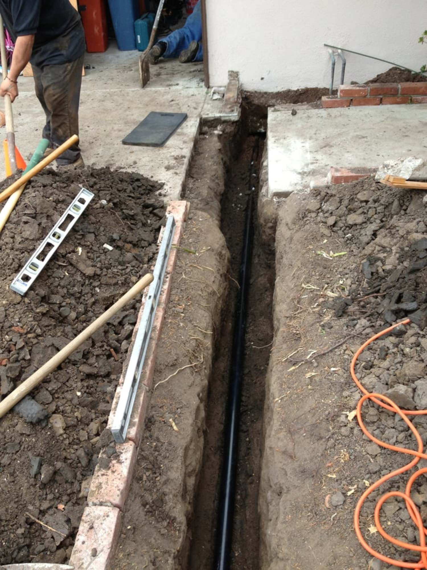 A man is digging a hole in the ground next to an orange cord