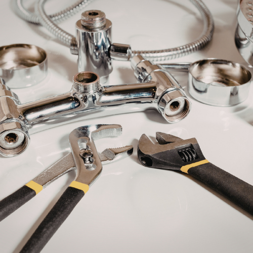 Plumbing tools, including tongue-and-groove pliers and an adjustable wrench, lying next to disassembled faucet parts.