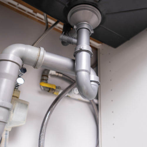 Gray plastic sink plumbing pipes, including a P-trap, installed beneath a kitchen or bathroom sink.