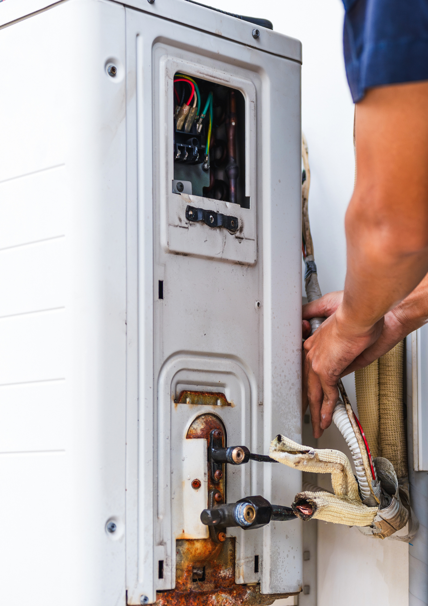 A technician works on the wiring and connections of a white outdoor air conditioning unit.