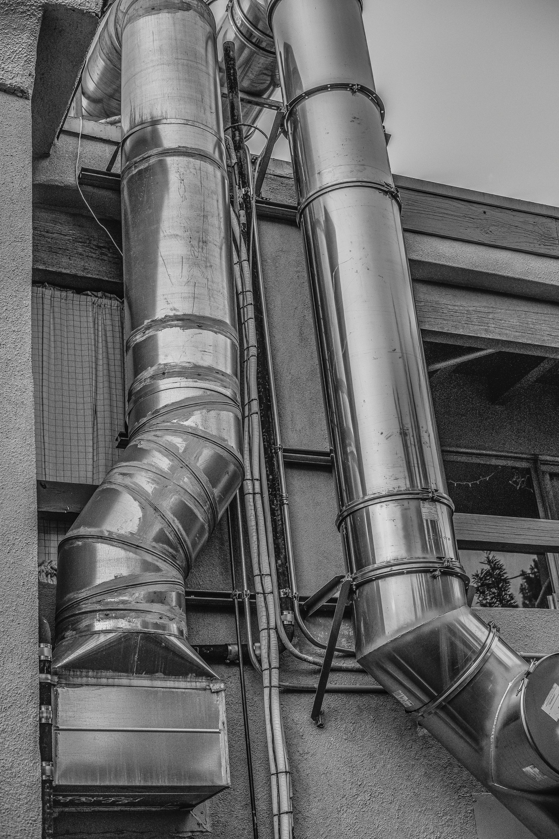 Two large, industrial metallic ventilation ducts run vertically along a textured, concrete building wall.