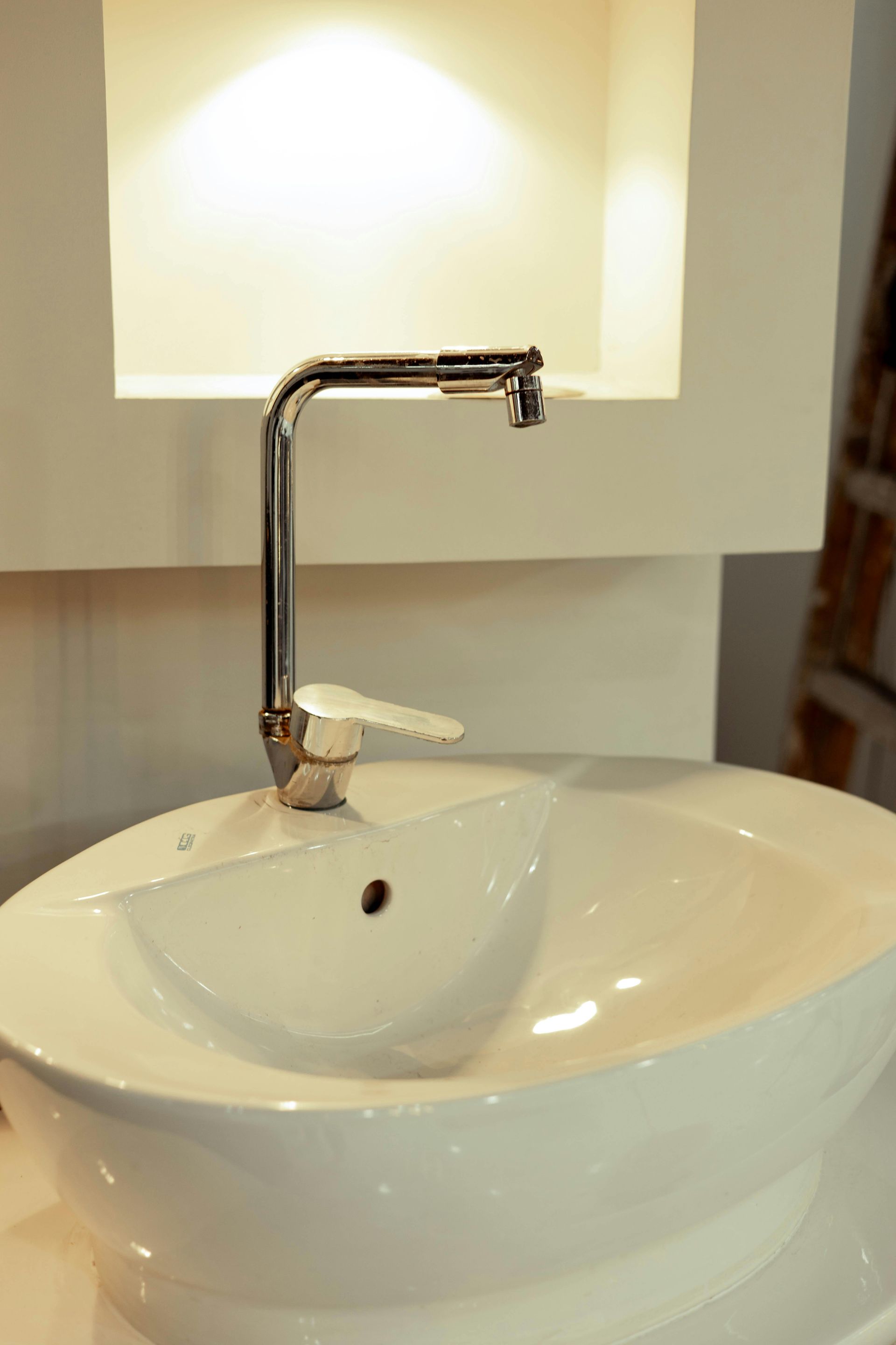 A modern white oval vessel sink with a chrome faucet, set against a white wall with a recessed niche.