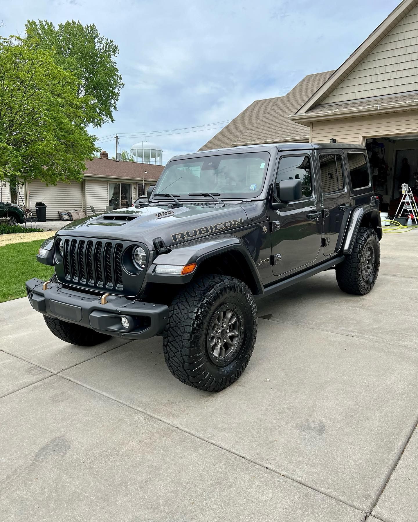 Gray Jeep Wrangler Rubicon parked on a driveway in front of a house.