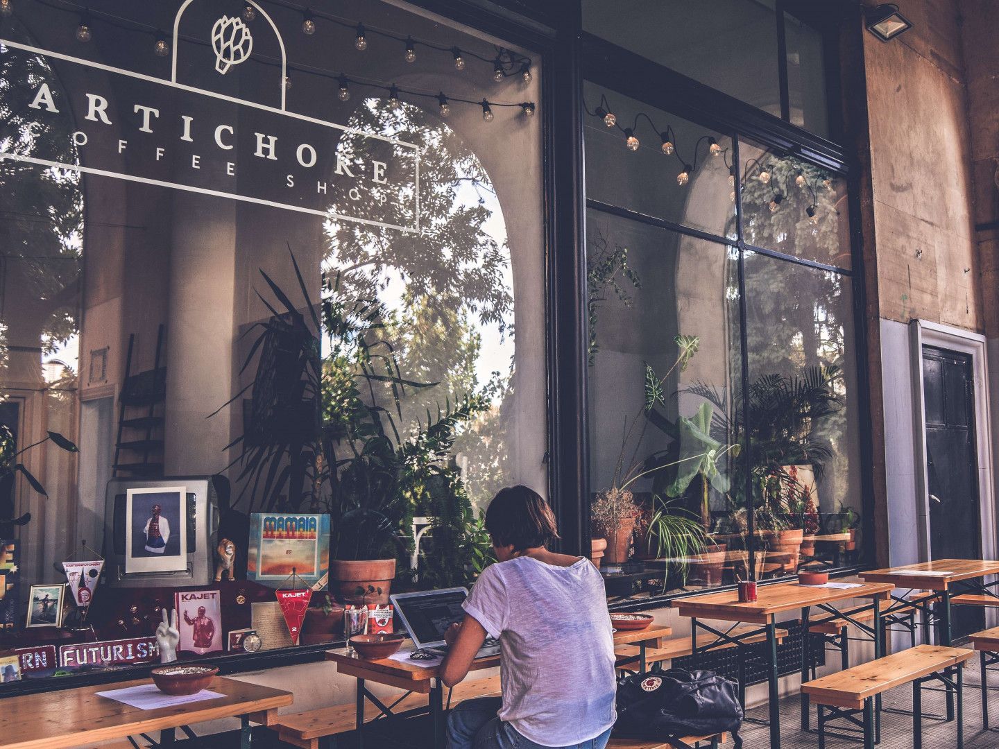 A woman sits at a table in front of a restaurant called artichoke