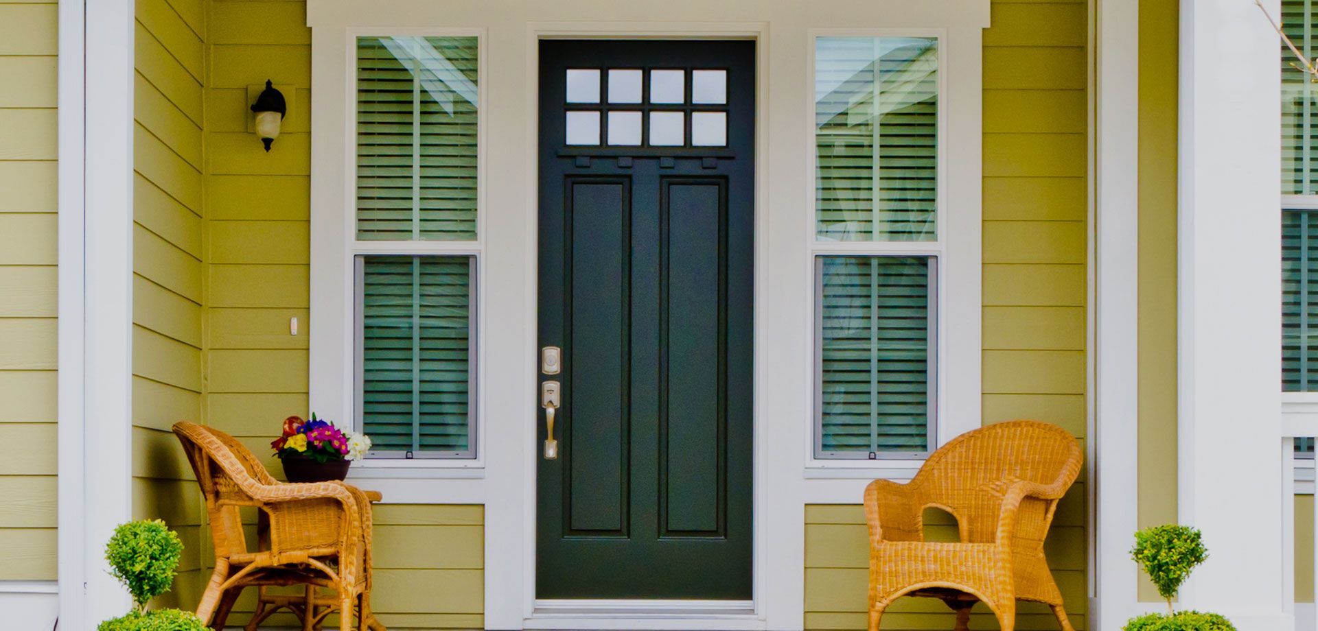 A yellow house with a black door and wicker chairs on the porch.