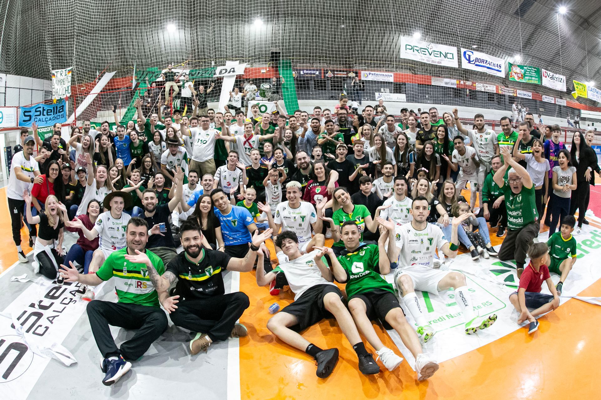 Um grande grupo de pessoas está posando para uma foto em quadra, torcedores, jogadores, comissão técnica, diretoria e apoiadores, celebrando a conquista.