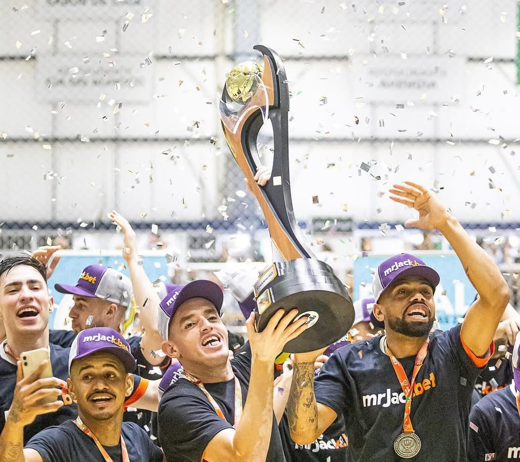 Grupo de jogadores celebrando em quadra com troféu em mãos.