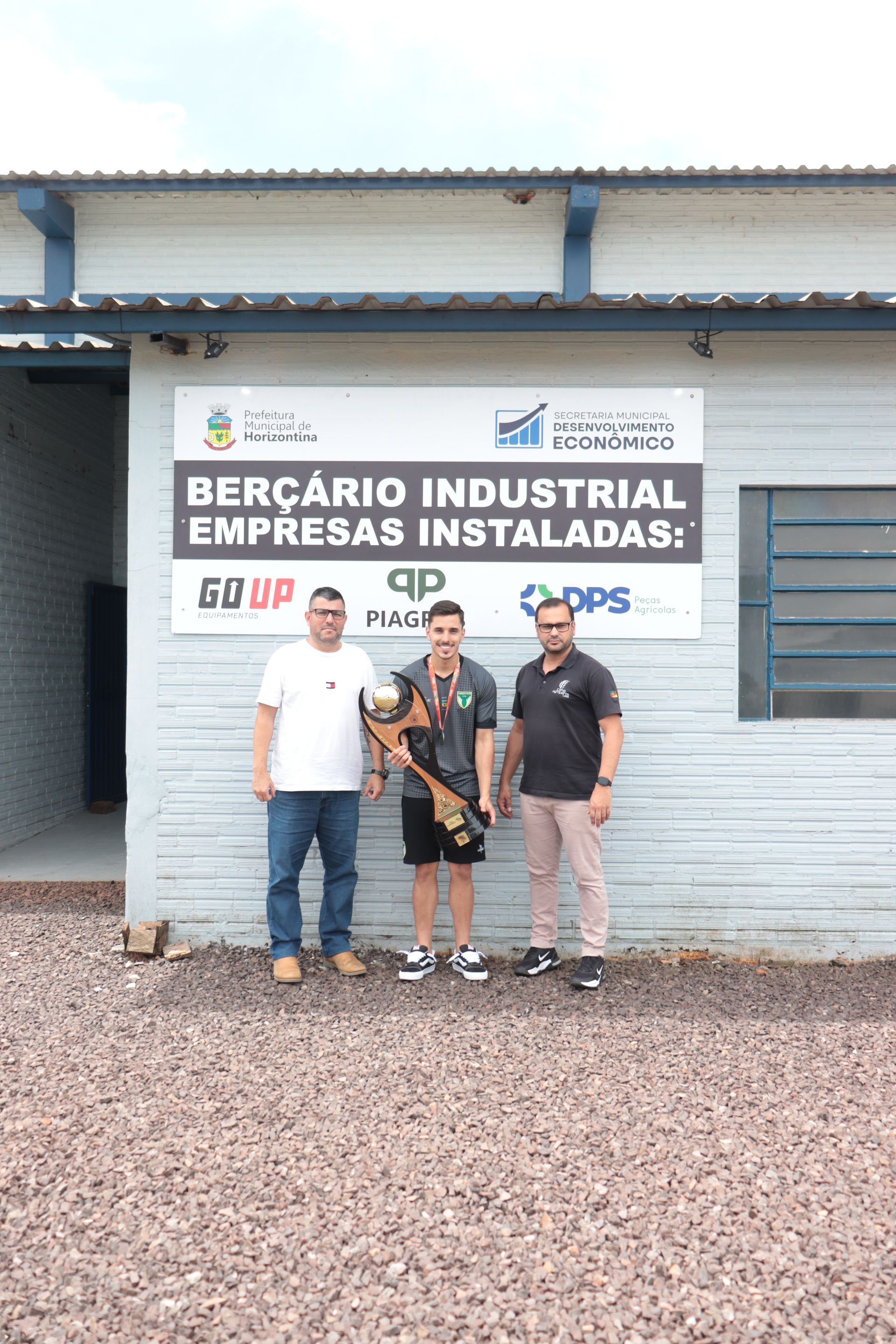 Três homens estão parados em frente a um prédio segurando um troféu.