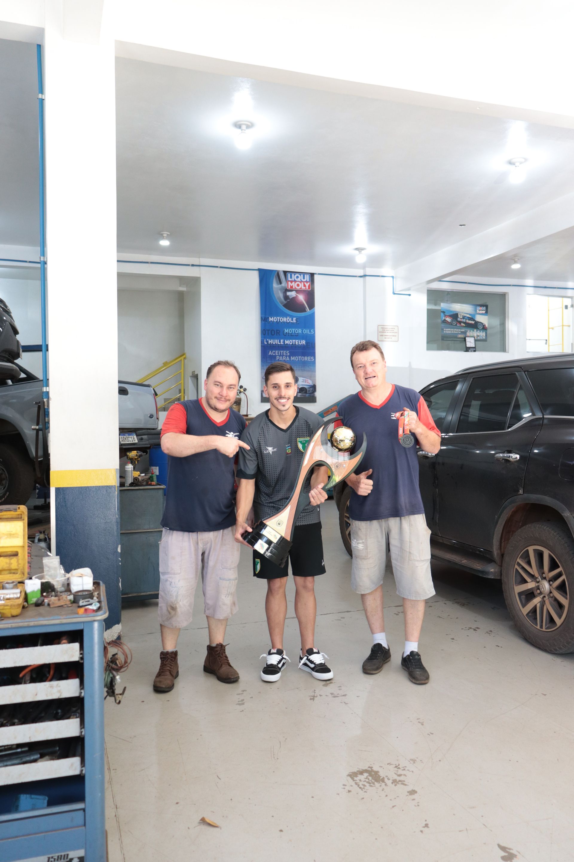 Três homens estão posando para uma foto em uma garagem.