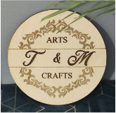 Ein Holzschild von T & M Crafts steht auf einem Tisch neben einer Pflanze.