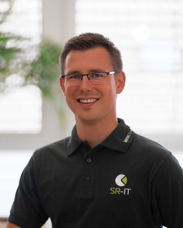 Ein Mann mit Brille und schwarzem T-Shirt mit der Aufschrift SR-IT