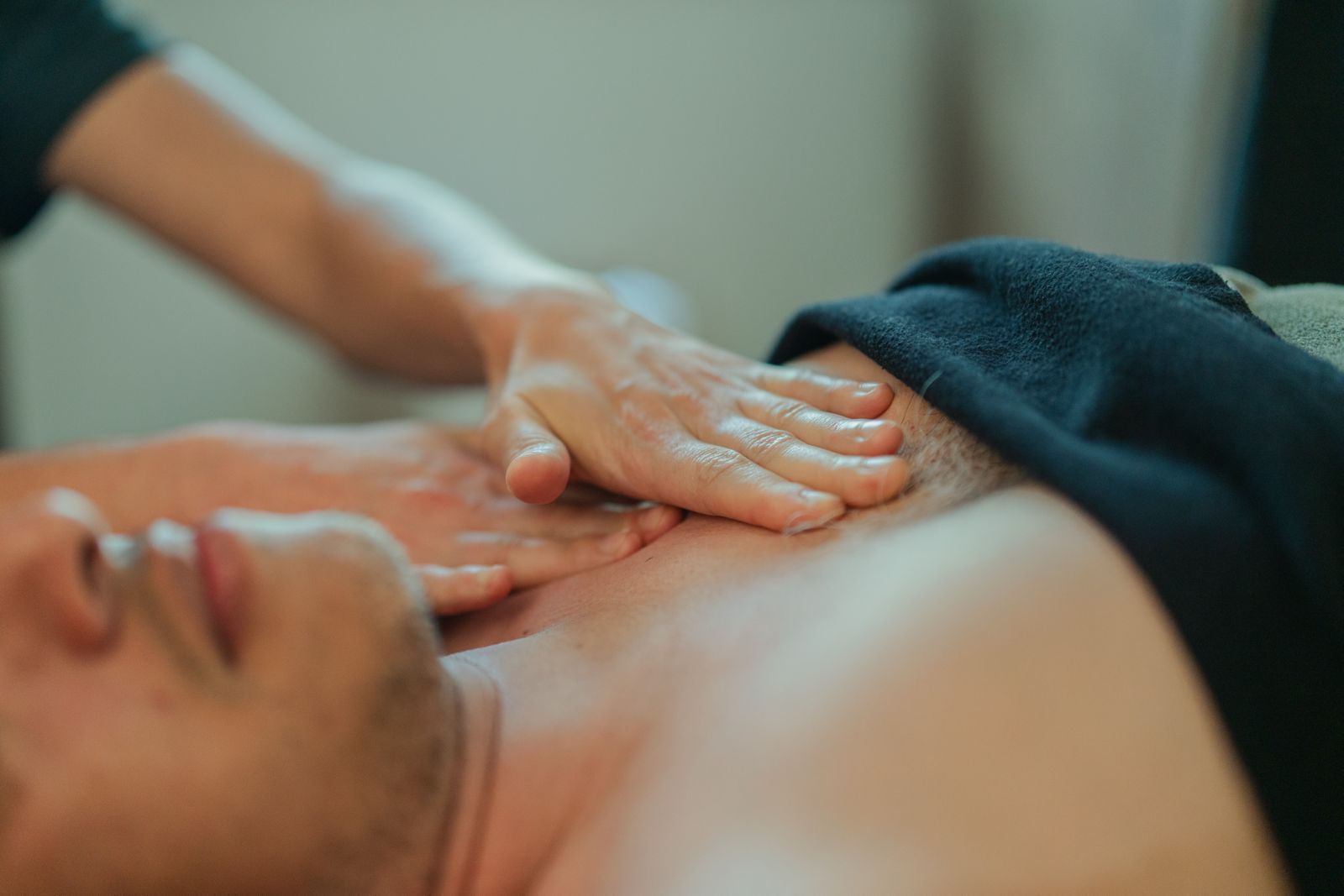 Des mains appuient sur le haut du dos d'une personne lors d'un massage, une serviette sombre se trouvant à proximité.