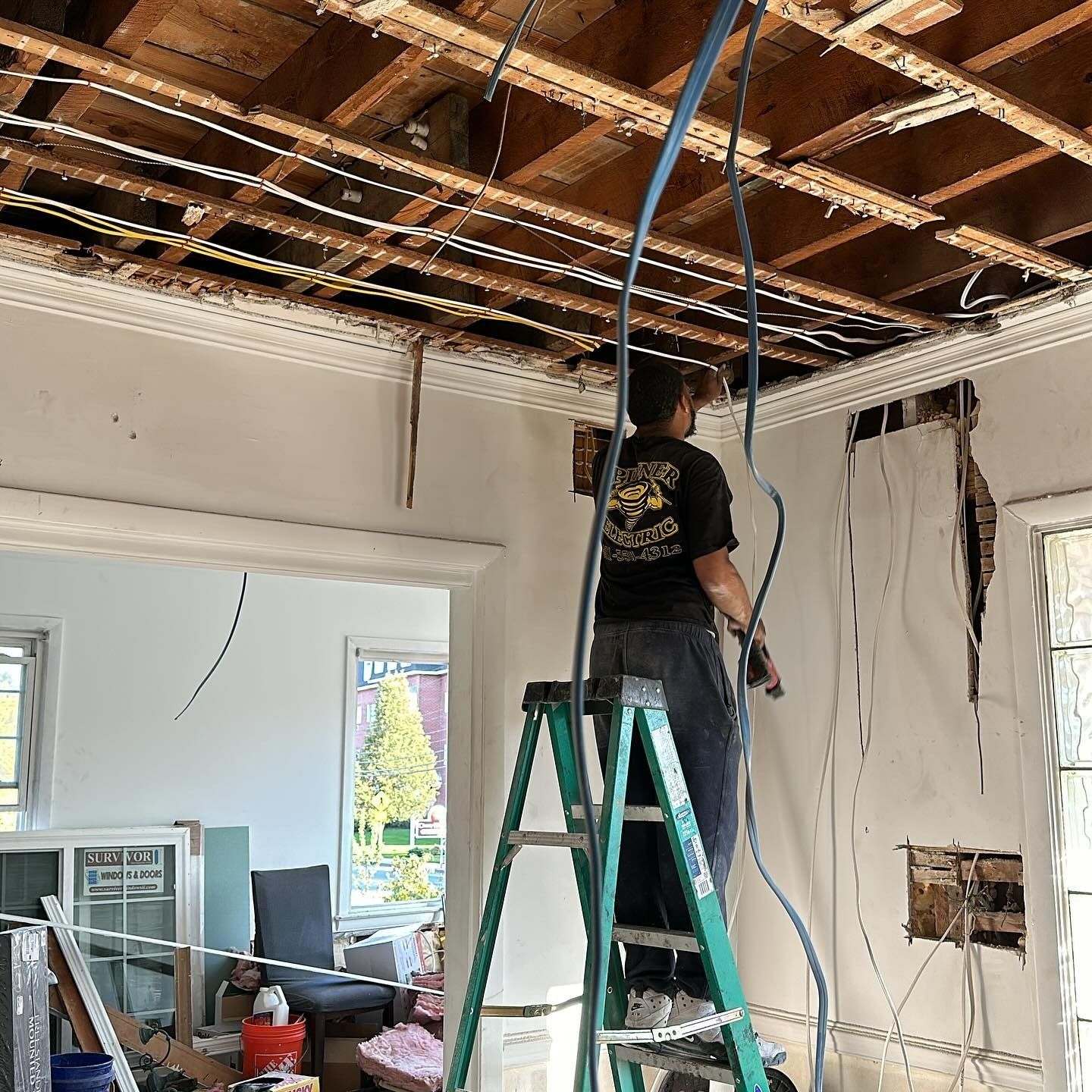 A man is standing on a ladder working on the ceiling of a house.