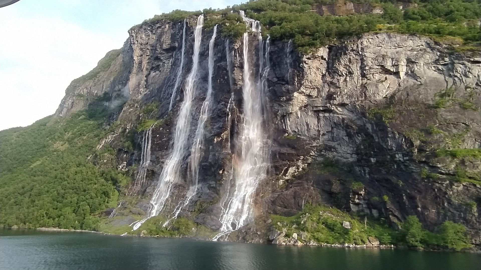 Een waterval aan de zijkant van een berg naast een fjord