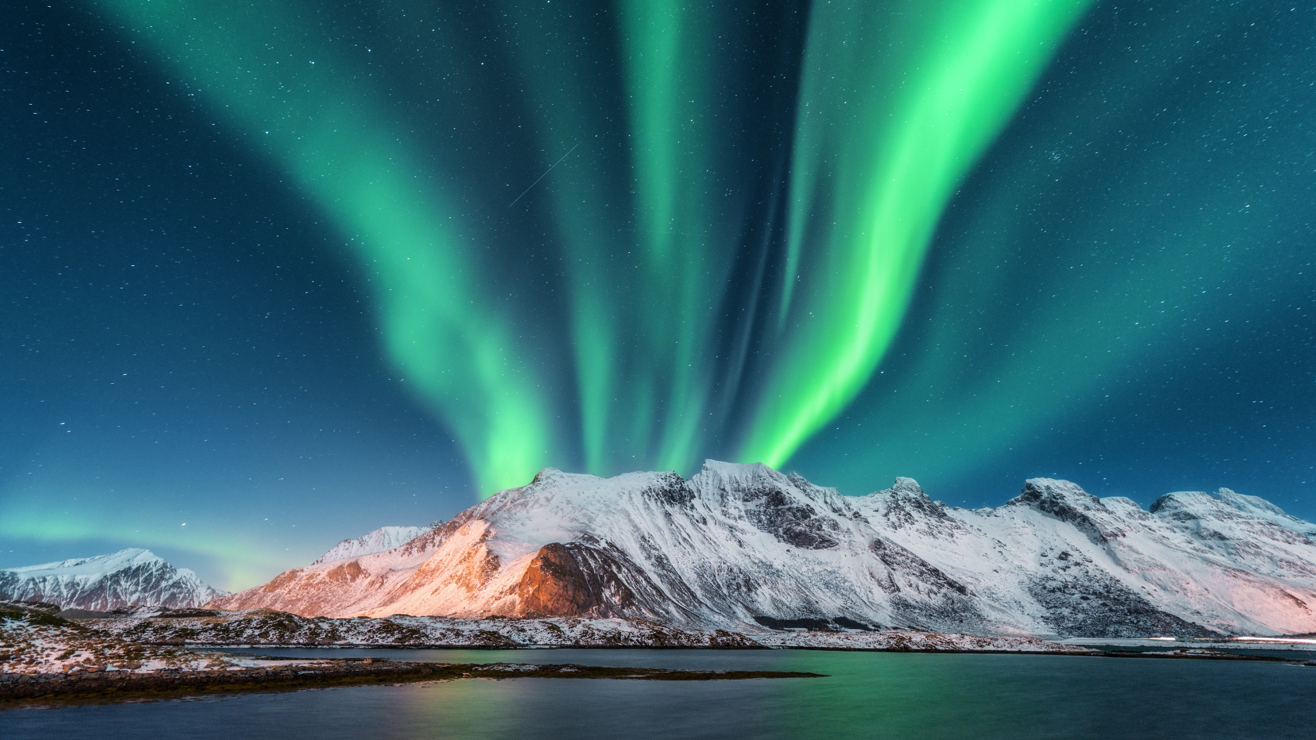 Het levendige groene noorderlicht verlicht de nachtelijke hemel boven met sneeuw bedekte bergen en een kalm, donker wateroppervlak.