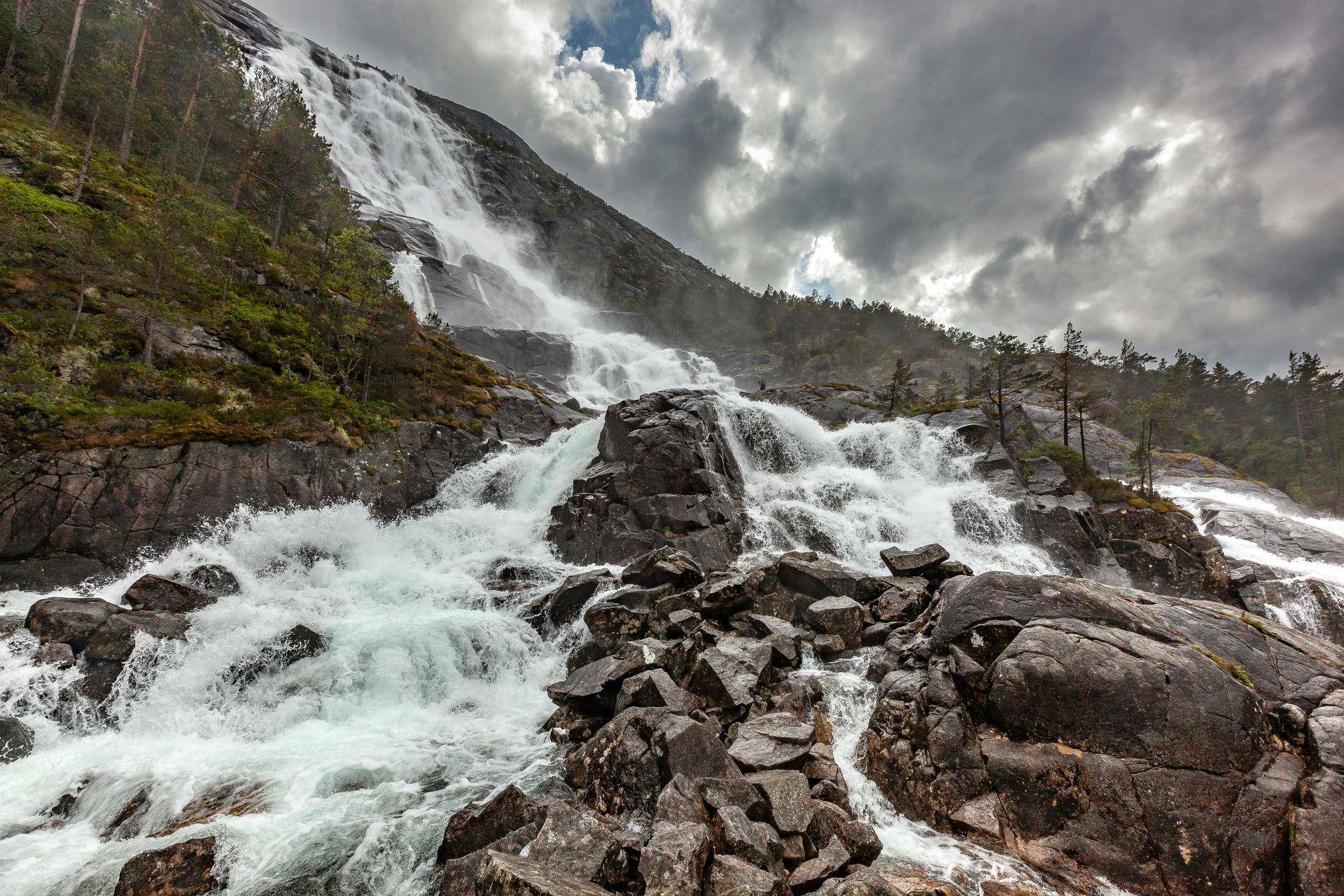 Een waterval is omgeven door rotsen en bomen op een bewolkte dag.