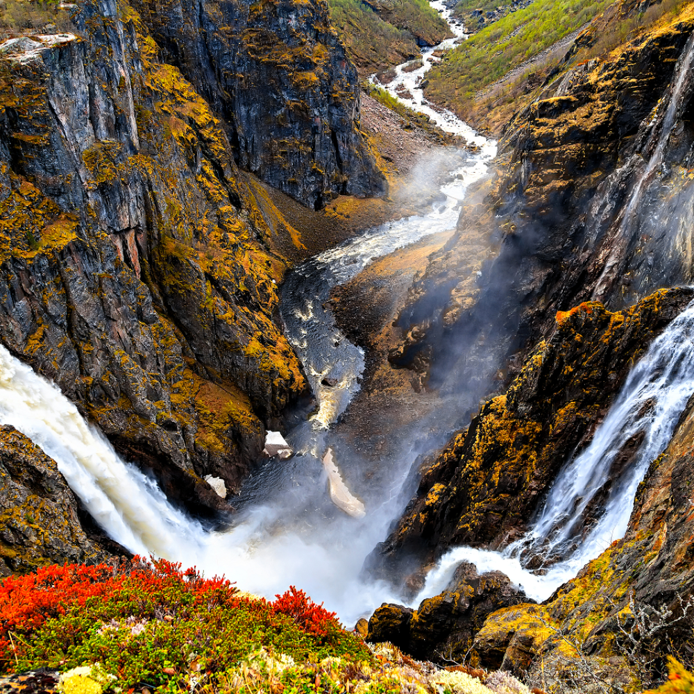 Een brede kloof met ruige kliffen, felrode begroeiing en twee majestueuze watervallen die samenkomen in een centrale rivier.