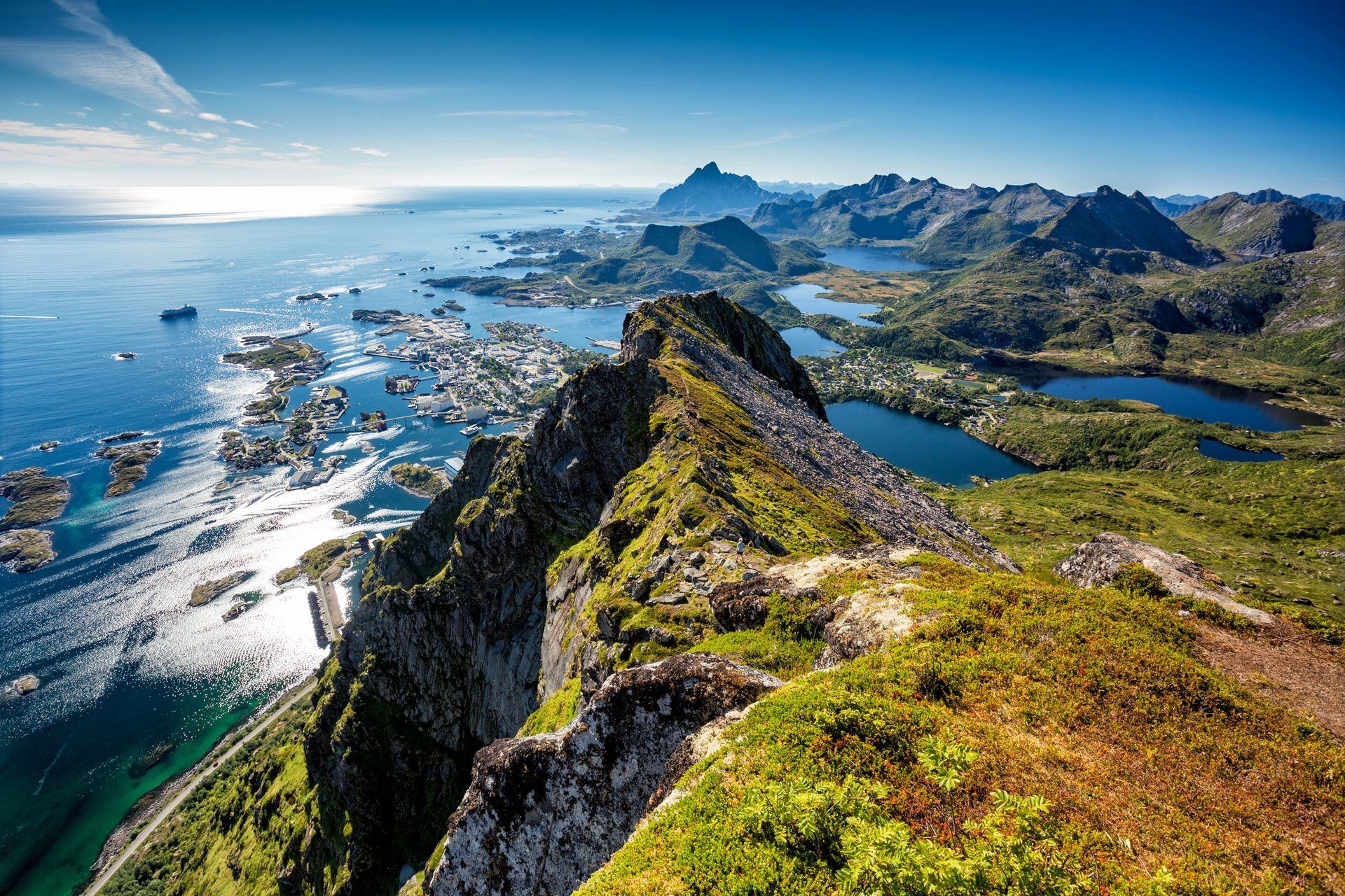 Luchtfoto van een indrukwekkende, ruige bergkam met uitzicht op een kustplaats, kleine eilanden en diepblauwe fjorden.