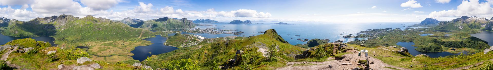 Panoramisch uitzicht op weelderige groene bergen die een diepblauwe kustbaai omringen onder een heldere, deels bewolkte hemel.