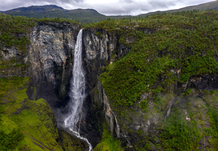 Een luchtfoto van een waterval in de bergen, omgeven door bomen.