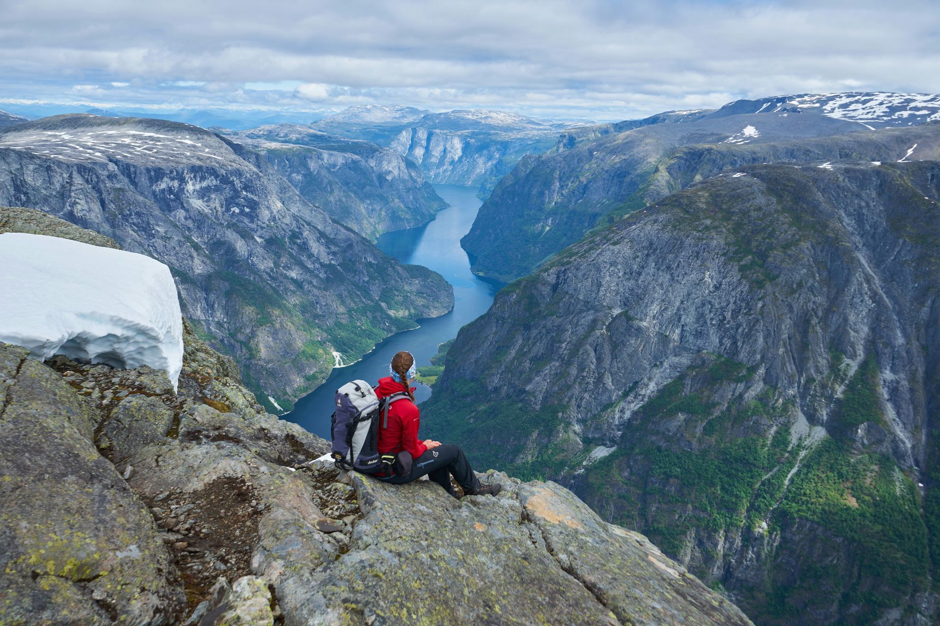 Iemand zit op de rand van een klif met uitzicht op een fjord.