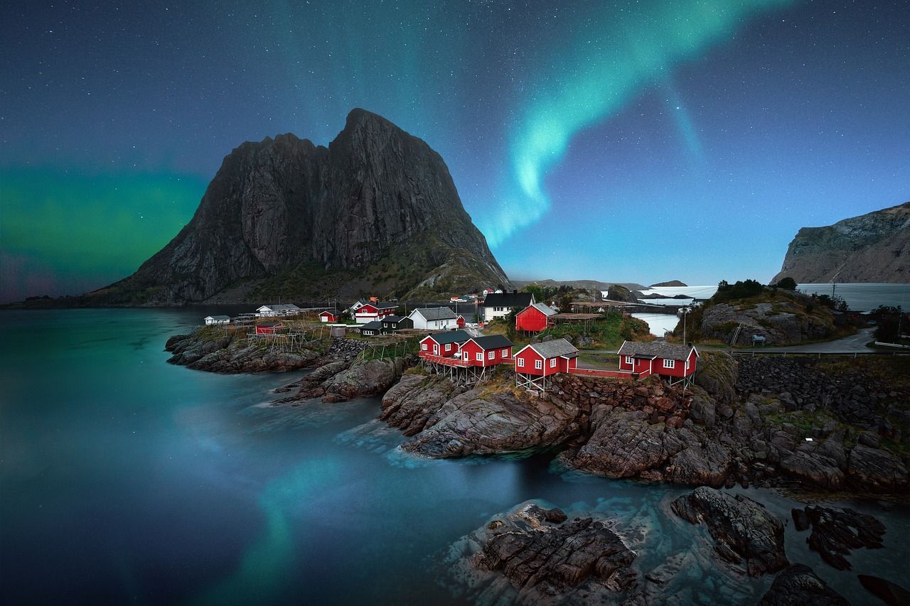 Het noorderlicht schijnt over een klein dorpje aan de oever van een fjord.
