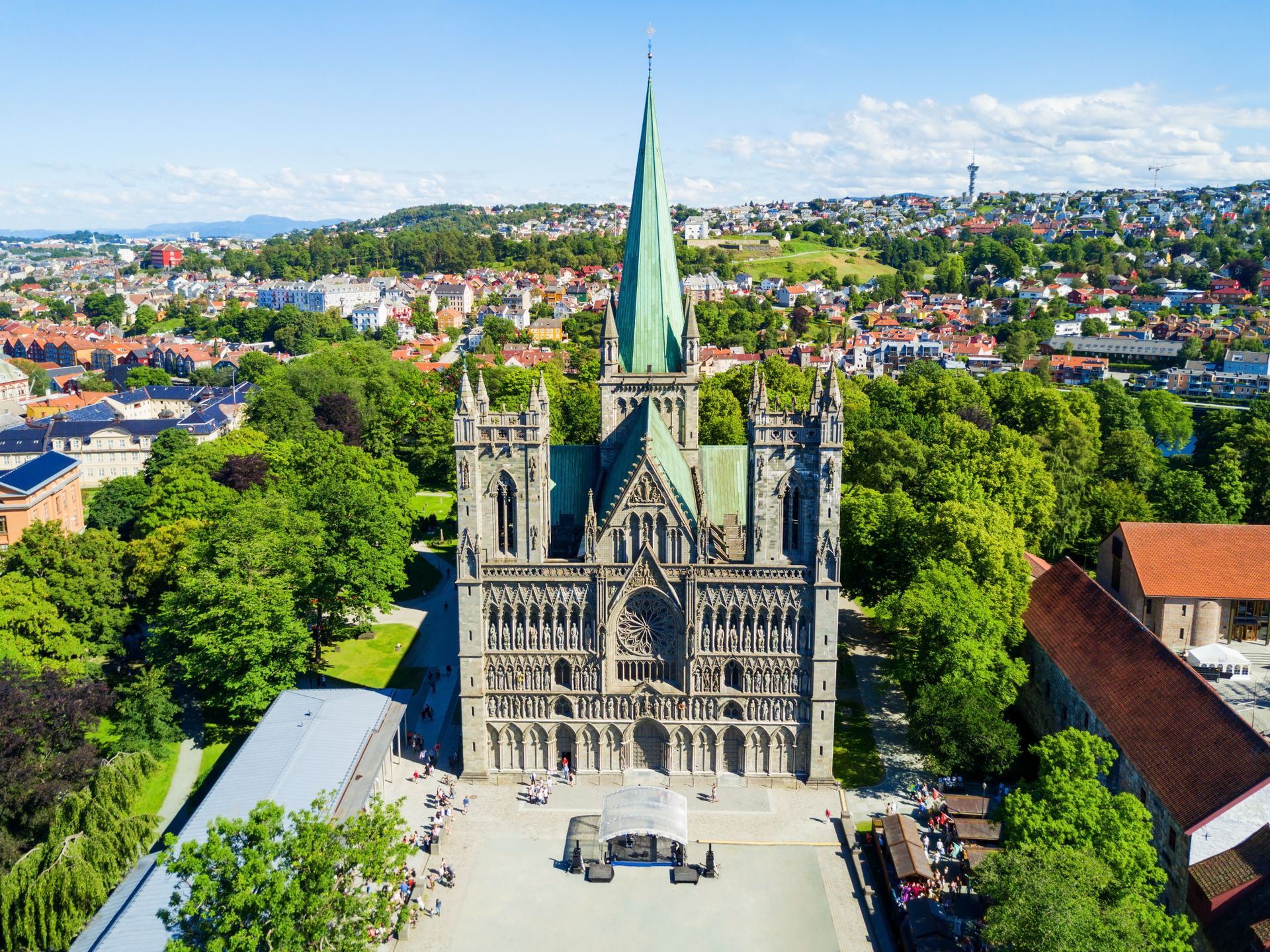 De Nidaros-kathedraal in Trondheim, Noorwegen, met een opvallende groene torenspits en een sierlijke stenen gevel te midden van weelderige groene bomen.