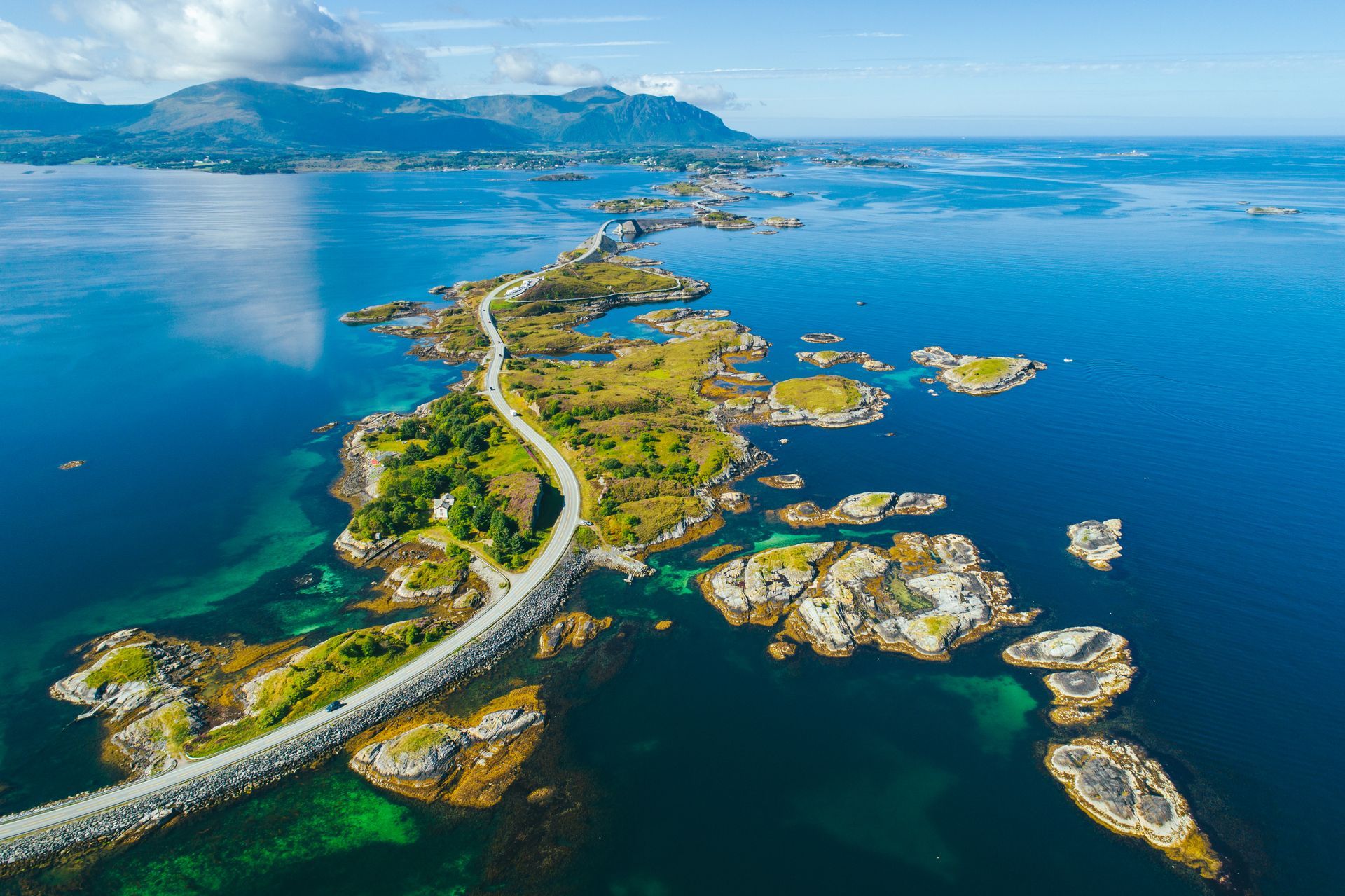 Luchtfoto van de Atlantische Oceaanweg in Noorwegen, met een kronkelende weg die kleine, groene, rotsachtige kusteilanden met elkaar verbindt.