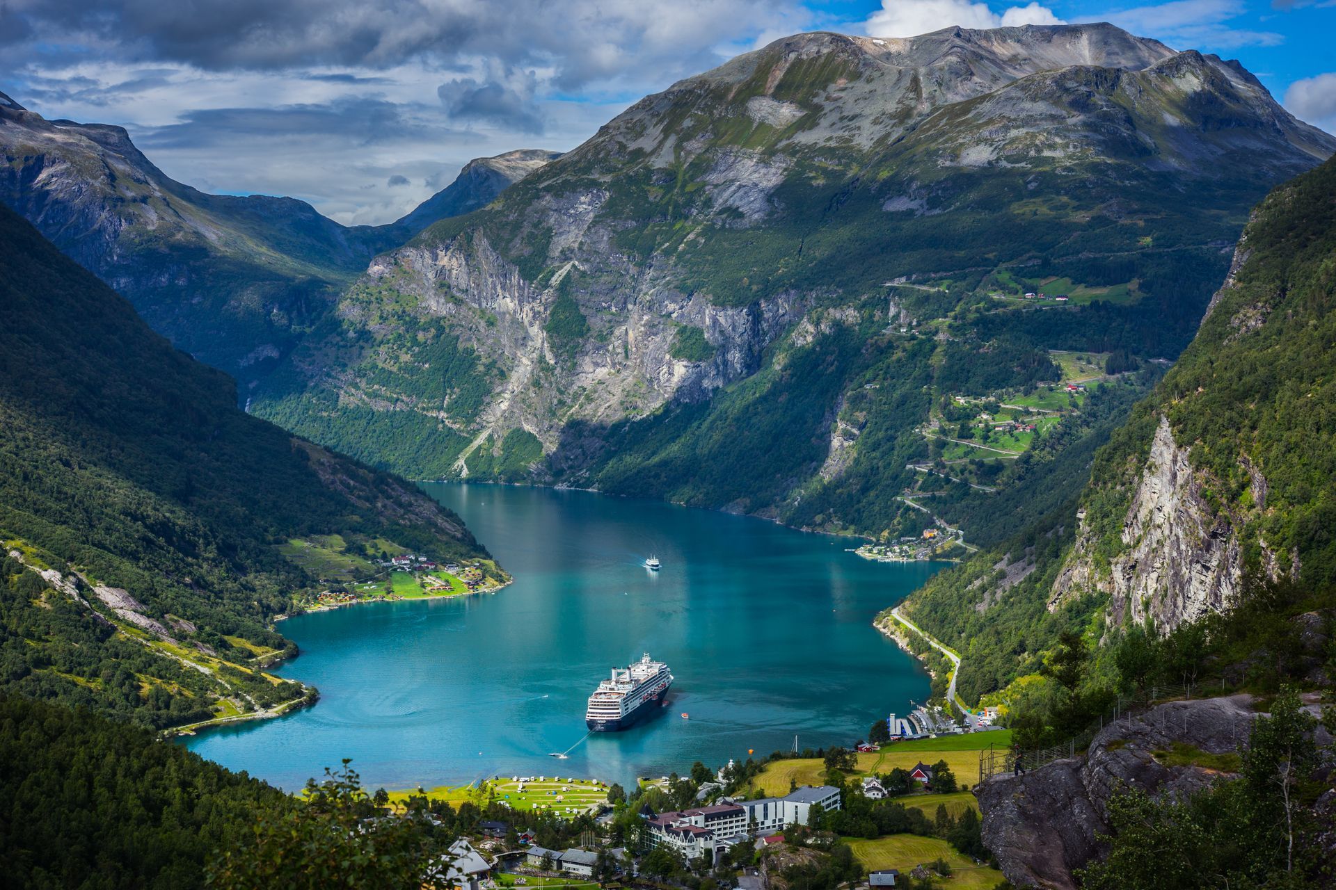 Een groot cruiseschip vaart over het diepblauwe water van de Geirangerfjord, omgeven door weelderige groene bergen en kliffen.