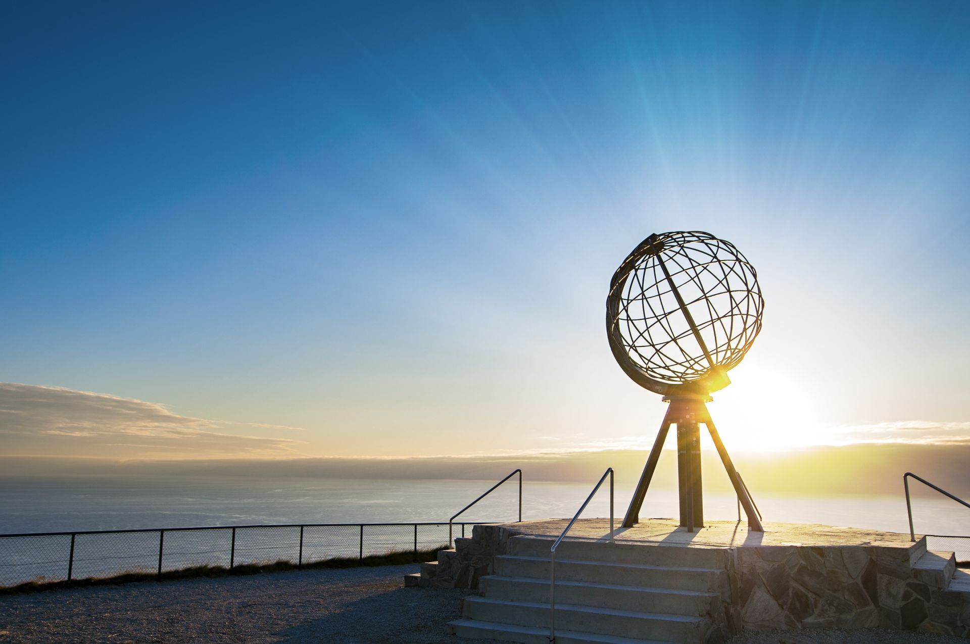 Een metalen bolsculptuur op een platform biedt uitzicht op de oceaan onder een heldere, zonnige hemel bij de Noordkaap in Noorwegen.