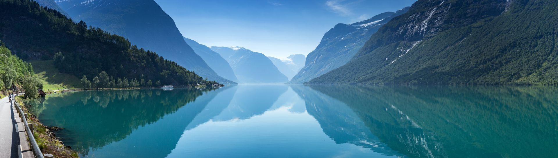 Een panoramisch uitzicht op een kalm turkooizen meer, verscholen tussen steile, beboste bergen onder een helderblauwe hemel.