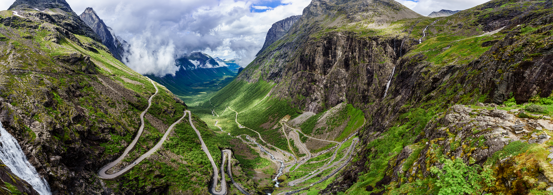 Een luchtfoto van een bergvallei met een weg erdoorheen en een waterval.
