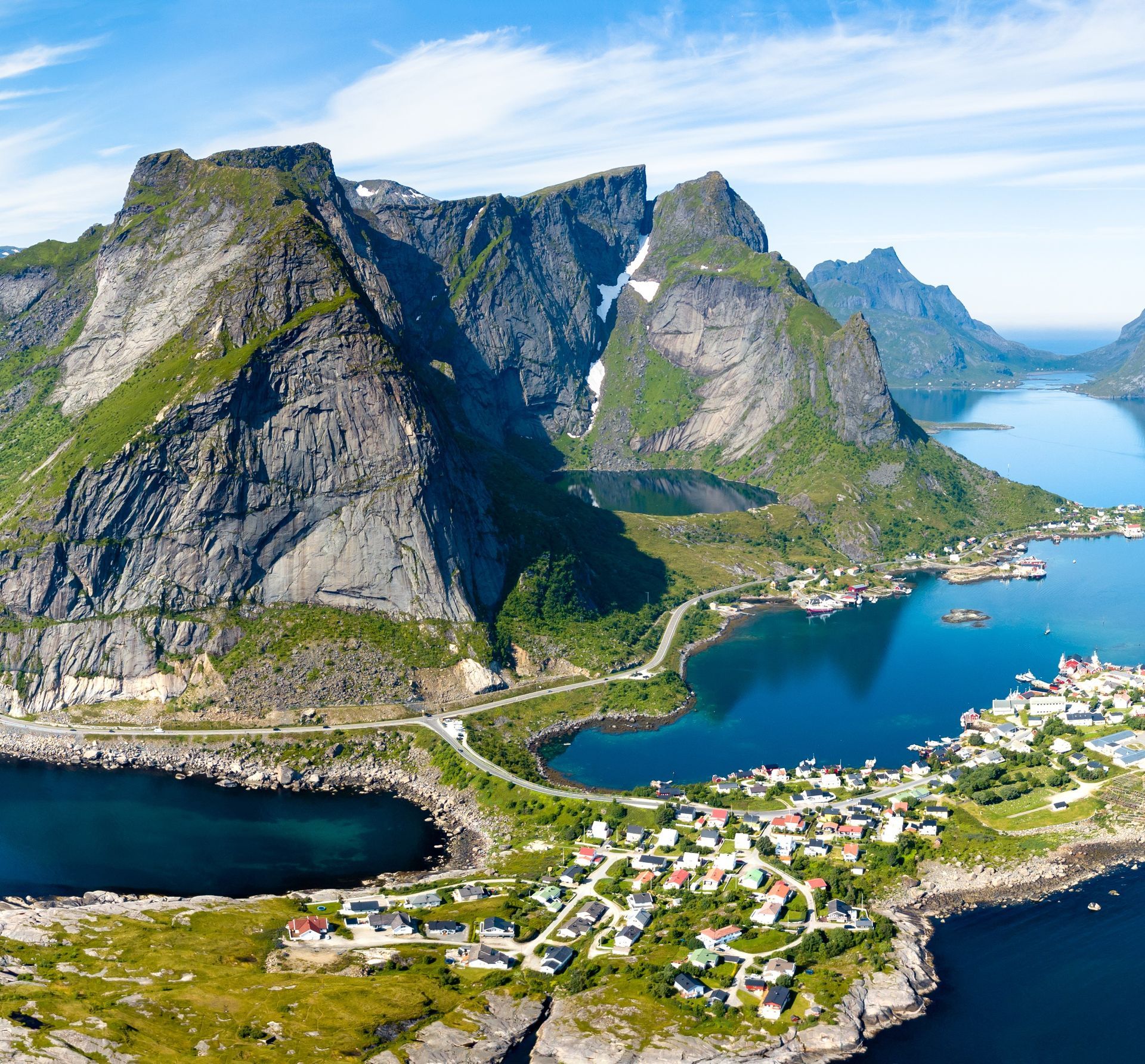 Een kustdorp met kleurrijke huizen, verscholen tussen steile, grillige bergen en diepblauwe oceaanfjorden onder een zonnige hemel.