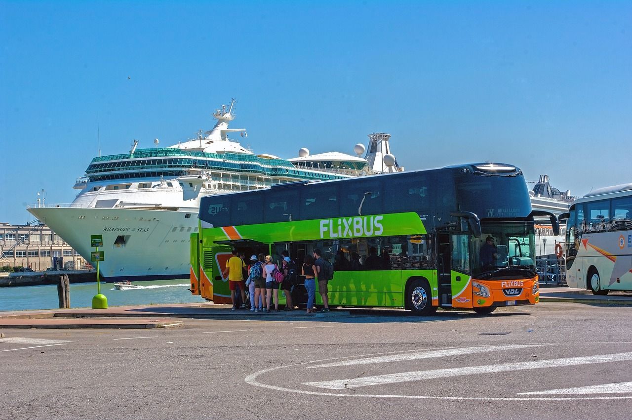 Een groene FlixBus-dubbeldekker staat geparkeerd in een cruisehaven, met passagiers die aan boord gaan vlakbij een groot wit cruiseschip.