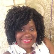 Woman with curly black hair smiles widely, wearing red lipstick and a white top.