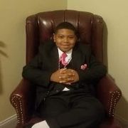Young boy in a suit sitting in a leather armchair, smiling.