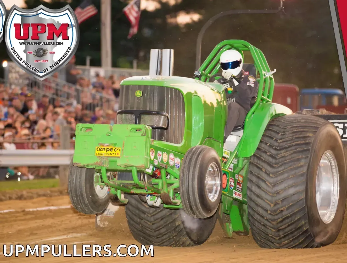 A green modified tractor pulling competition, with the front wheels lifted off the dirt track in front of a crowd.