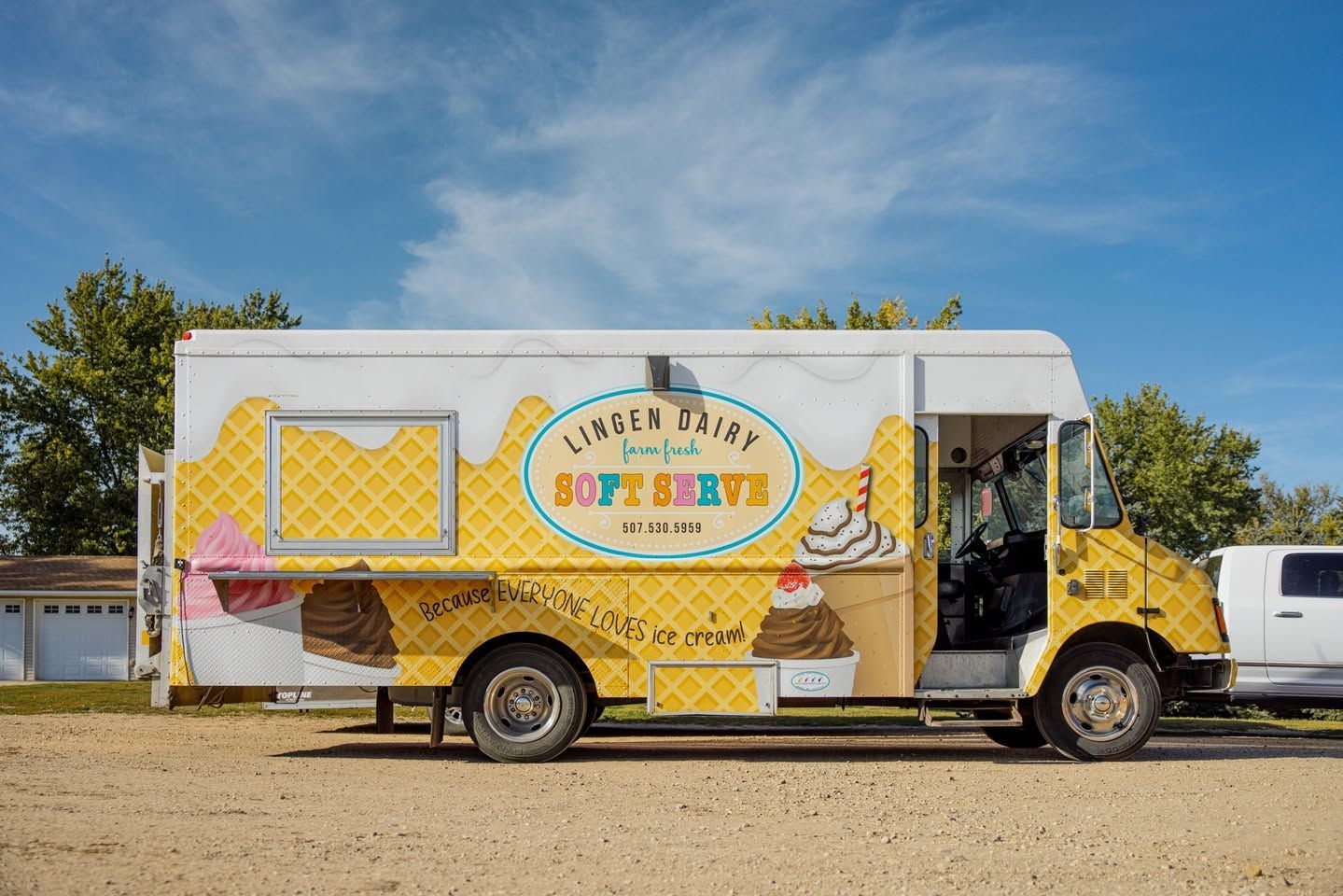 A yellow and white ice cream truck parked outdoors under a blue sky, featuring a logo that reads 