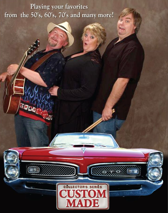 Four musicians in black cowboy hats and suits stand against a black background, posing with acoustic and electric guitars.