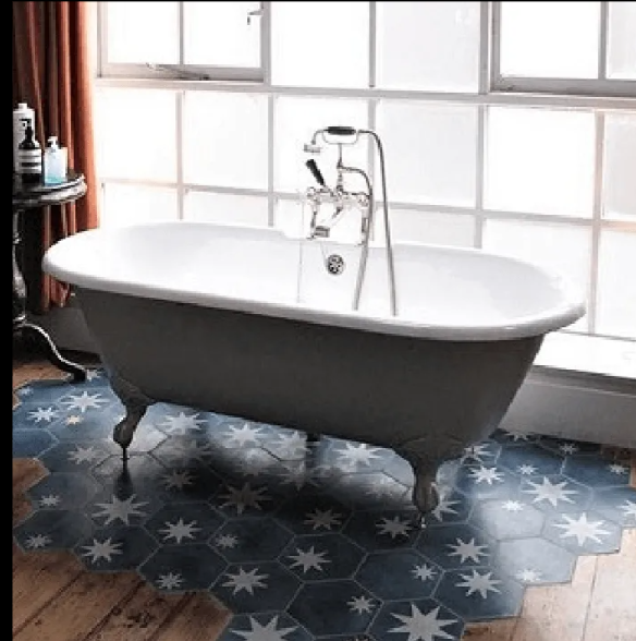 Bañera antigua con patas de garra en un baño luminoso con suelo de baldosas azules estampadas y grandes ventanales.