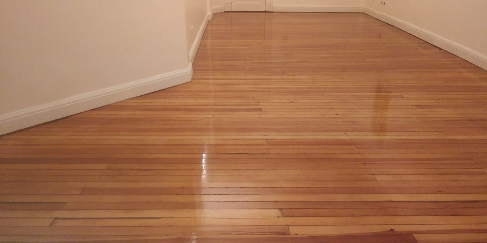 Pasillo vacío con suelo de madera recién pulido y paredes blancas.