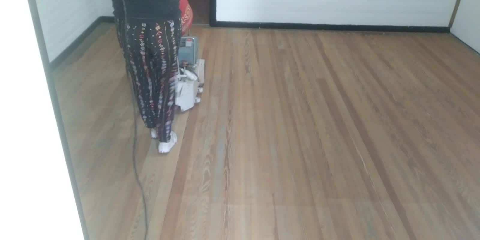 Una persona está de pie sobre un suelo de madera cerca de una pared con un electrodoméstico blanco y cables.