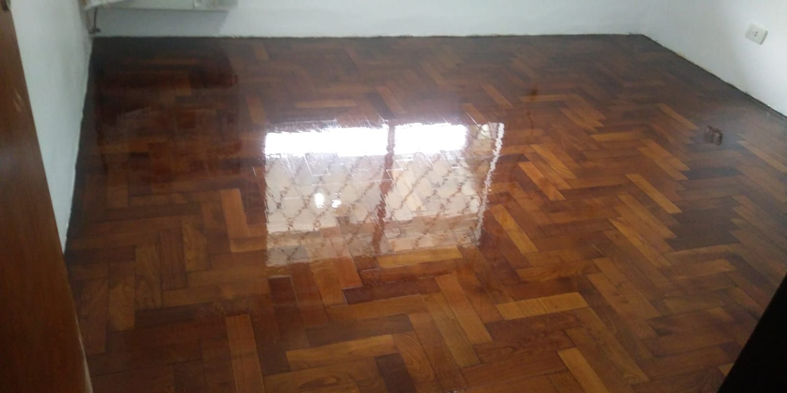 Suelo de madera pulida en una habitación vacía con reflejos de una ventana.