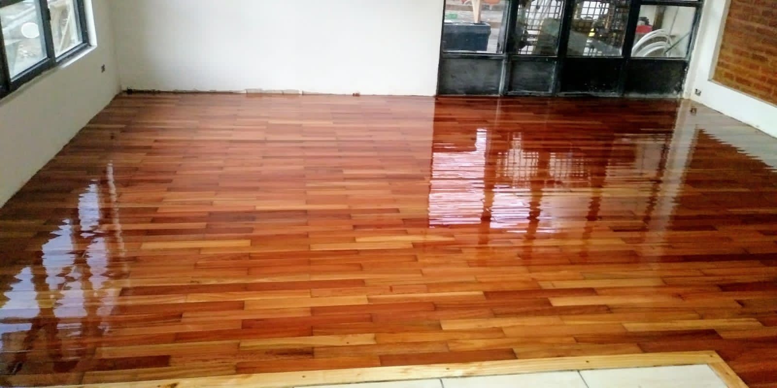 Habitación vacía con suelo de madera noble pulida y brillante y ventanas que reflejan la luz.