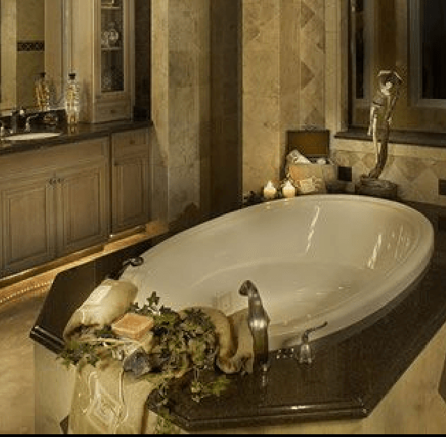 Elegante baño con una gran bañera ovalada, paredes de mármol y velas en la repisa.