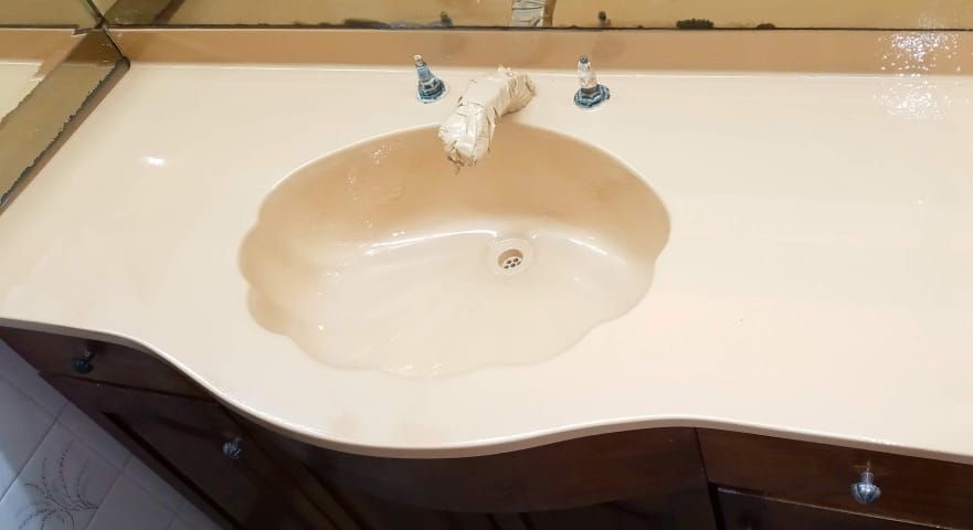 Lavabo de baño color crema integrado en un mueble de baño oscuro brillante con grifos cromados.